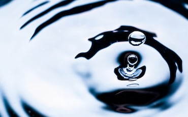 Close-up of a water droplet creating concentric ripples on a smooth surface. The image captures the droplet mid-splash in an inviting location, with reflections and shadows adding contrast to the liquid texture, reminiscent of tranquil amenities found in a serene oasis.