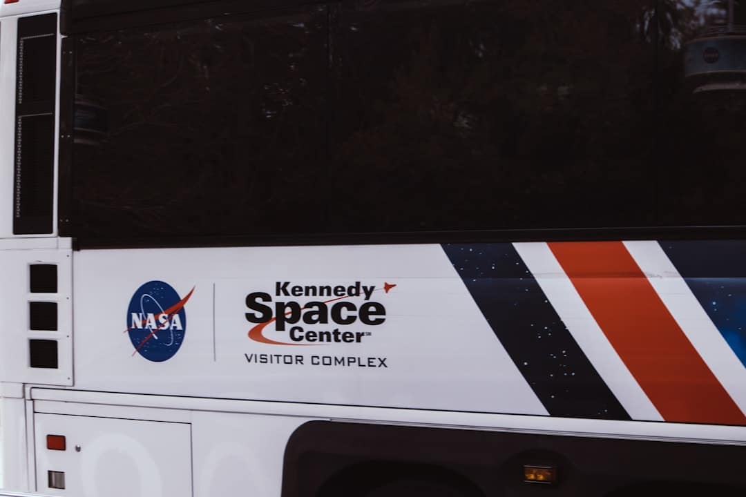 A bus with a NASA logo and "Kennedy Space Center Visitor Complex" written on the side. The design includes red, white, and blue stripes on the right.